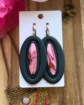 A pair of oval drop earrings with black outer frames and inset pink marbled faux stone centers