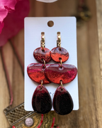 A pair of handmade dangle earrings with three organic shapes in a red ombré glitter design and small gold hoop closure