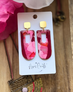A pair of statement earrings with rectangular ppendants filled with layered pink and red faux stone design, attached to gold square studs