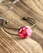 A cuff bracelet with an antique bronze finish and a round cabochon featuring pink and red faux stone